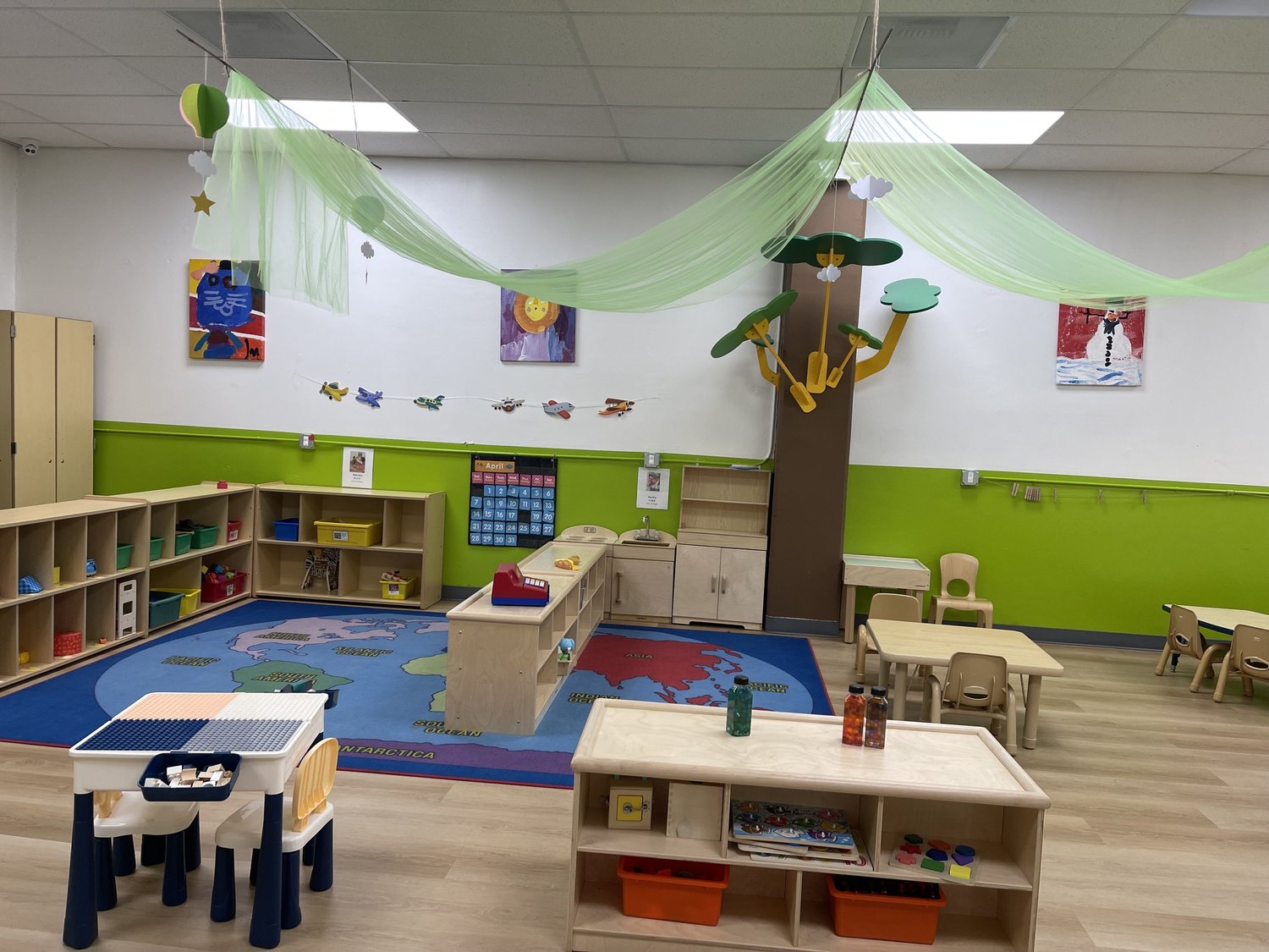 A toddler classroom at Apple Tree with wooden shelving and a green accent wall