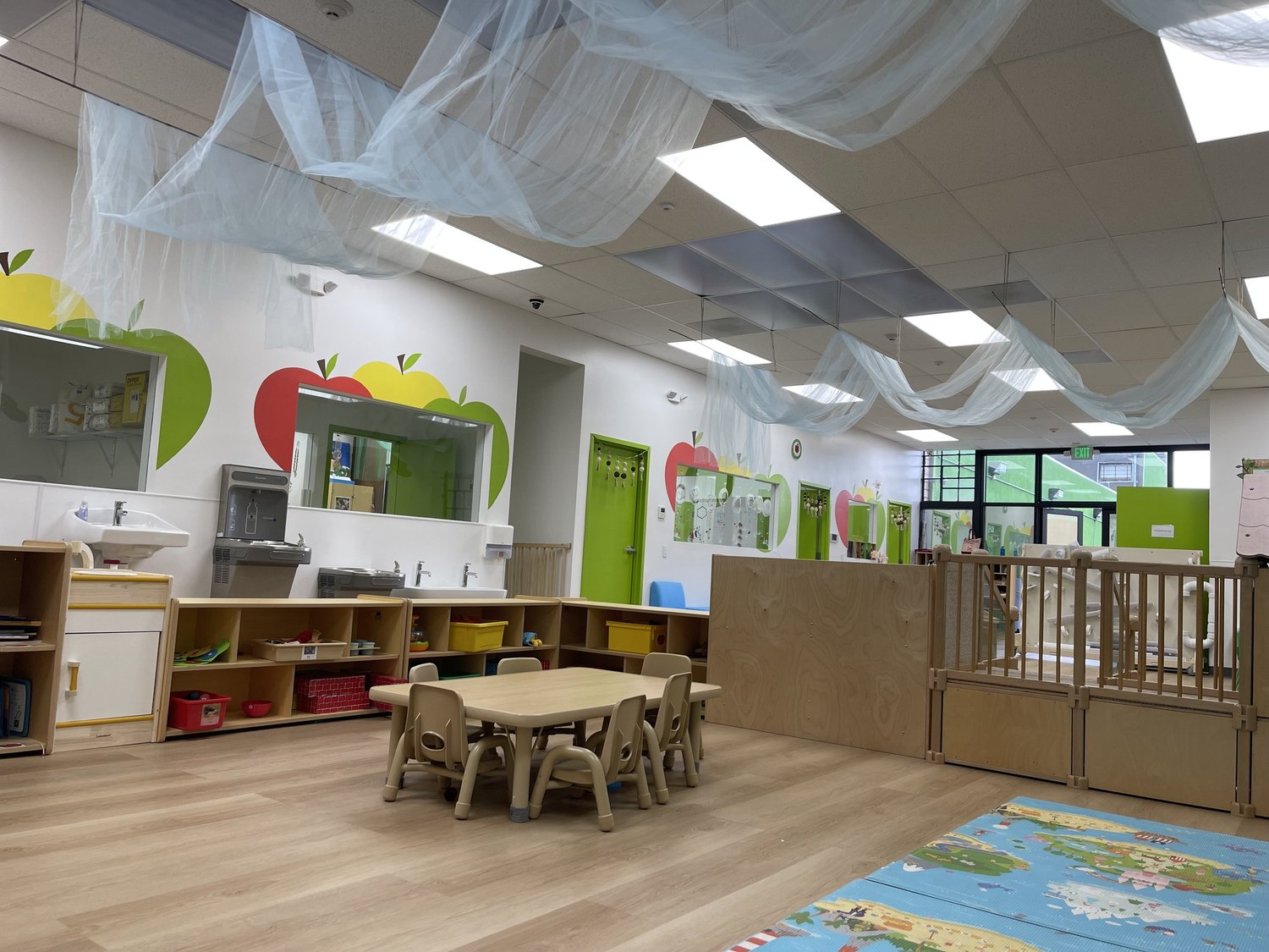 Apple Tree's open classroom with low wooden tables, child-height shelving and soft draped ceiling fabric