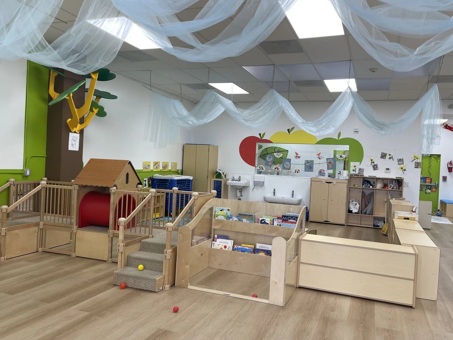 An Apple Tree classroom with a wooden climbing loft, open shelving and draped ceiling fabric