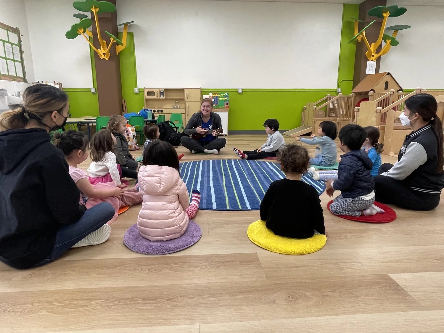 Apple Tree children and teachers gathered on the floor for circle time with a ukulele