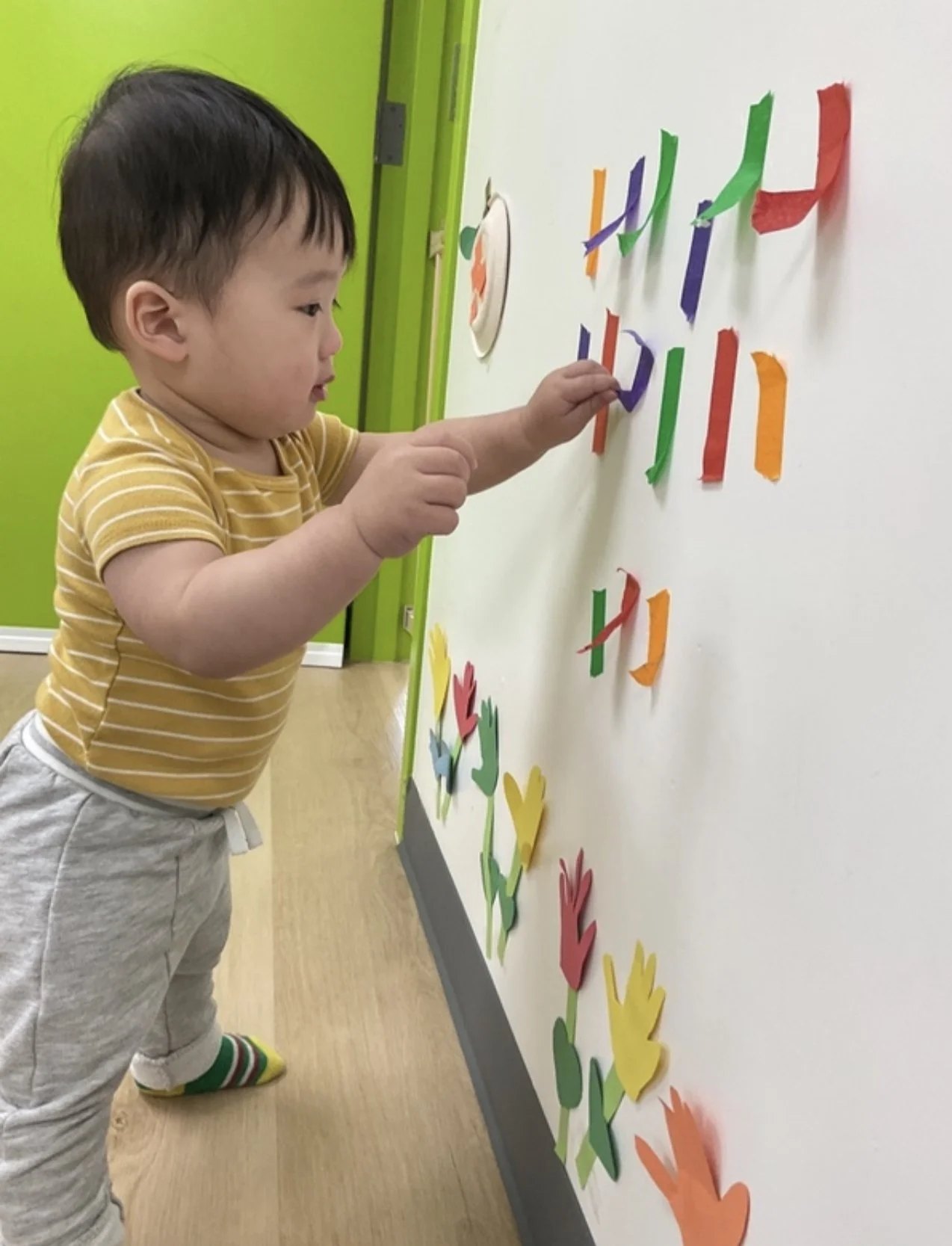 An Apple Tree child placing colourful letter cutouts onto a classroom wall
